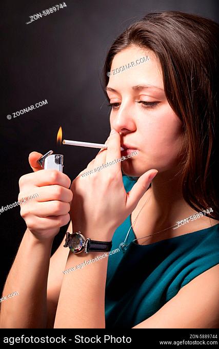 Beautiful young woman is smoking cigarette on black background