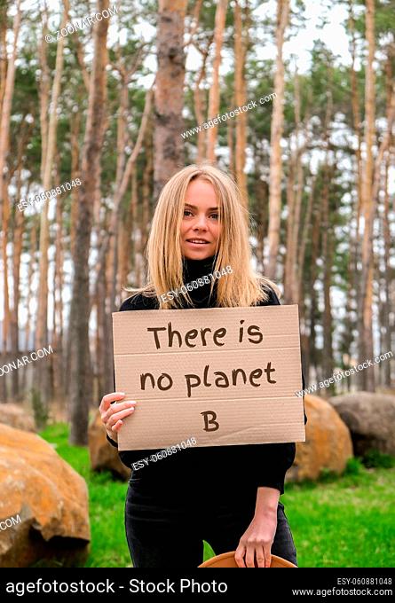 Portrait of caucasian young woman in hat holding cardboard with text outdoors. Nature background. Protester activist. Social activism