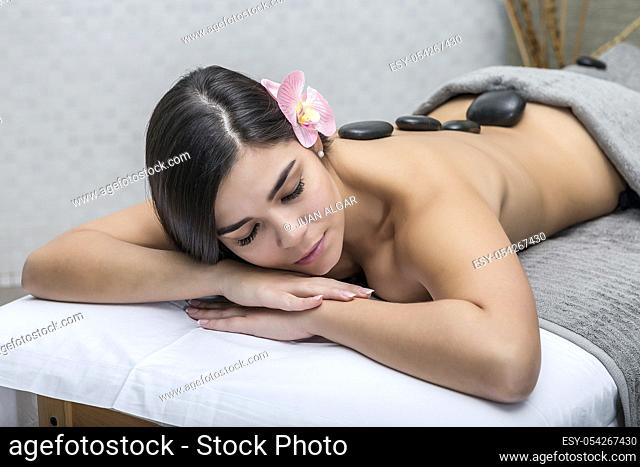 Alluring naked brunette with flower in hair lying on table in massage center