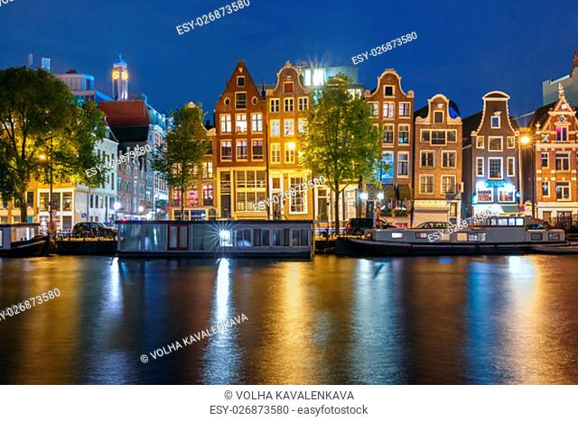 Amsterdam canal Amstel with typical dutch houses and houseboats with multi-colored reflections at night, Holland, Netherlands