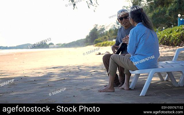 Happy senior couple relaxing outdoors singing and playing acoustic guitar at beach near sea sunny day, Mature man playing ukulele for his wife at sea
