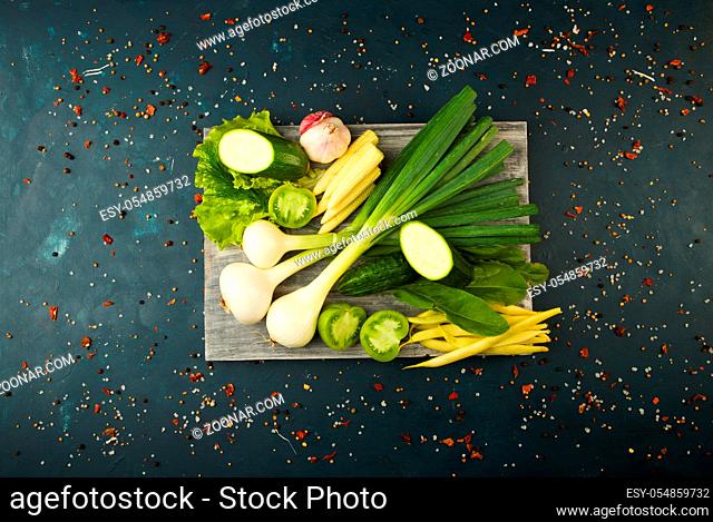 FRESH VEGETABLES AND SPICES ON A WOODEN BOARD ON A DARK STONE BACKGROUND. THE CONCEPT OF VINTAGE. SPICES THE YOUNG CORN ASPARAGUS GREEN TOMATO CUCUMBER ON A...