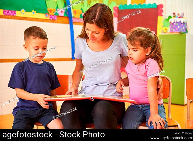 Erzieherin oder Tagesmutter beim Buch vorlesen für zwei Kinder in einer Kita oder Kinderkrippe
