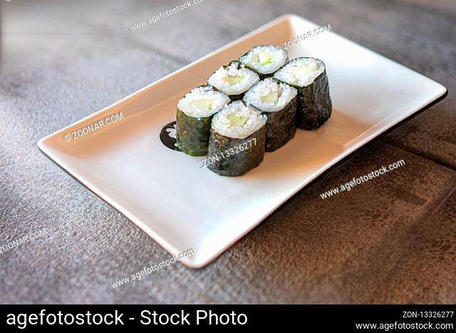 Cucumber Sushi served on rectangular white plate on dark gray stone background