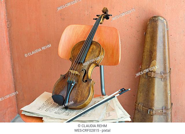 Violin, bow and sheet music on wooden chair with violin case in the background