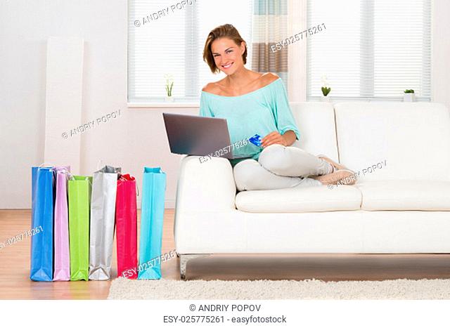Woman On Sofa Shopping Online With Shopping Bags In Living Room