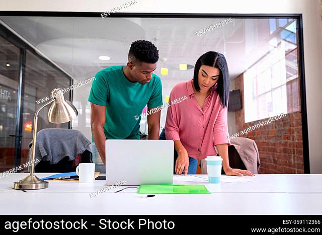 Diverse creative colleagues brainstorming in meeting room in front of laptop