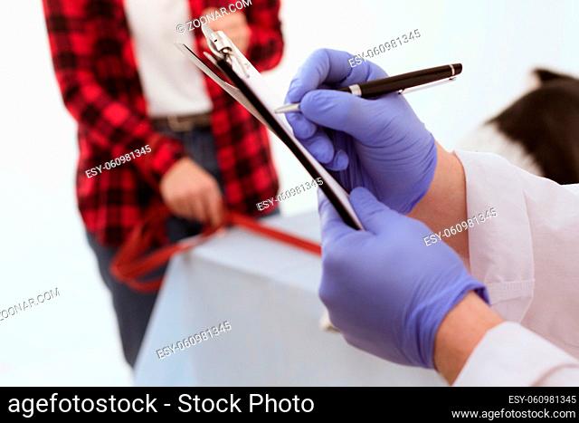 Veterinarian writing down notes on clipboard. Close up shot of doctors hands in blue rubber gloves holding clipboard and writing on it