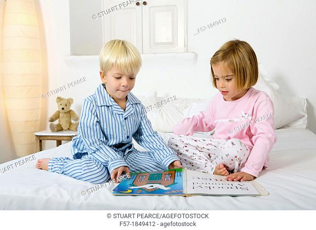 Siblings reading a book in their pyjamas
