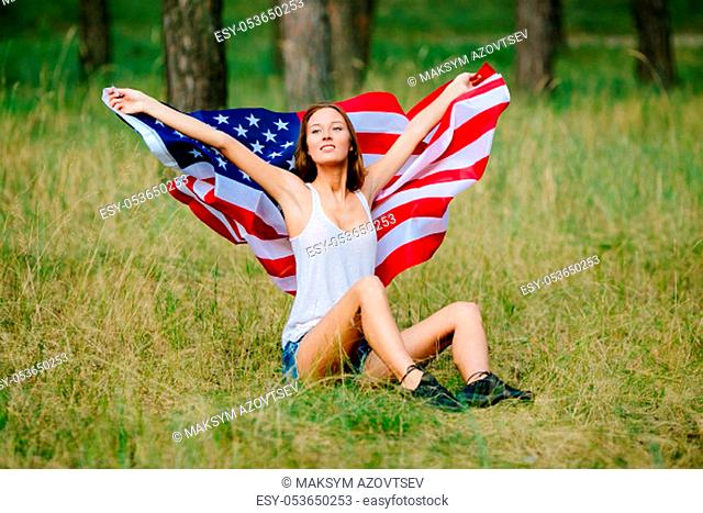 Happy girl is sitting on the grass with the American flag