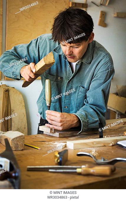 A craftsman using a piece of wood on the end of a chisel to mark a piece of wood
