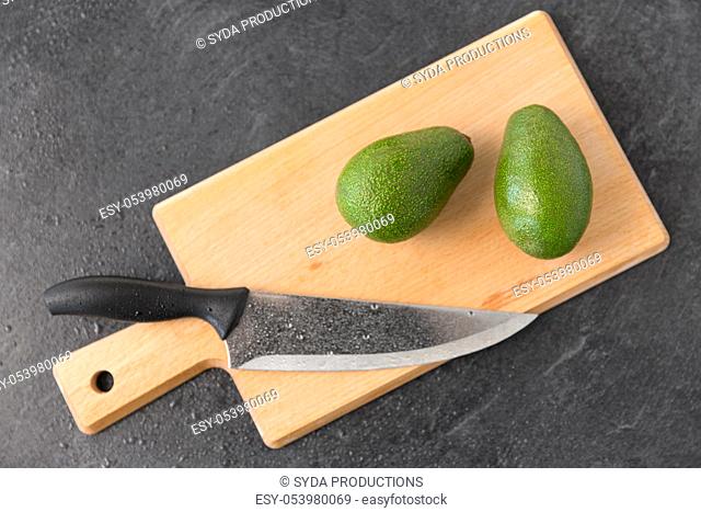 two avocados and kitchen knife on cutting board