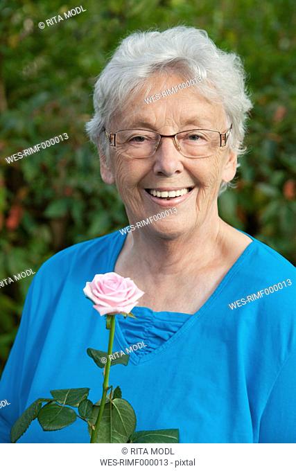 Germany, Bavaria, Huglfing, Senior woman with rose in garden, smiling, portrait