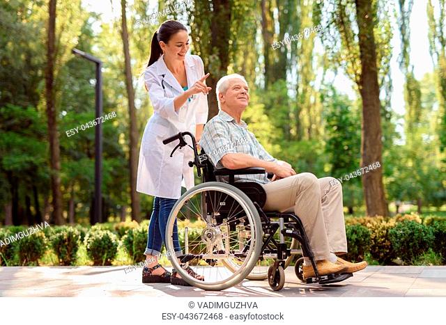 Happy old man in wheelchair in park with doctor