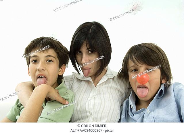 Mother and two sons sticking out tongues, one boy wearing clown's nose