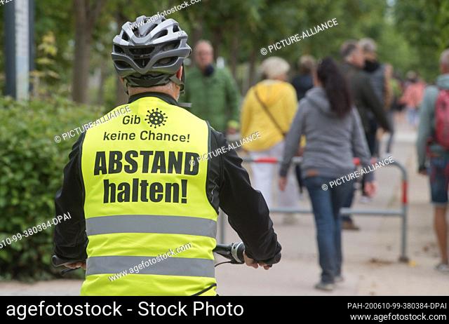 10 June 2020, Mecklenburg-Western Pomerania, Heringsdorf: A tourist wearing a safety vest with the inscription ""Keep your distance!"" drives along the beach...