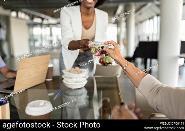 Businesswoman giving salad box to senior colleague at desk