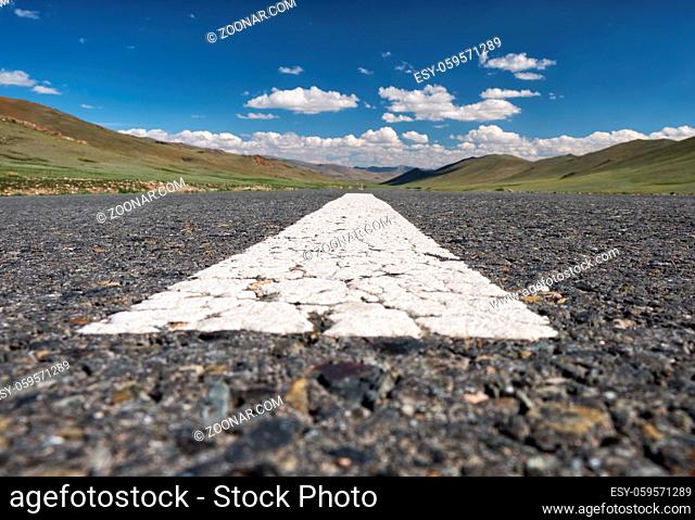 Wide-angle shot of empty road markings on asphalt in Mongolia between mongolian towns Tsagaannuur and Bayan-Olgii under blue sky