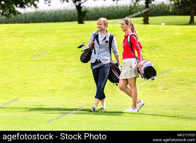 Portrait of happy golfing couple with golf bag on green field