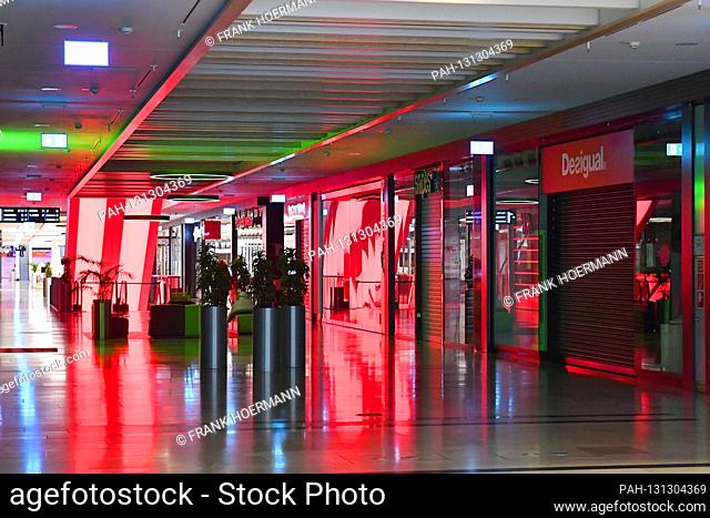 Empty aisles and escalator-closed shops, shops, shops bathed in red light. Closed shopping mall due to corona pandemic, shopping center