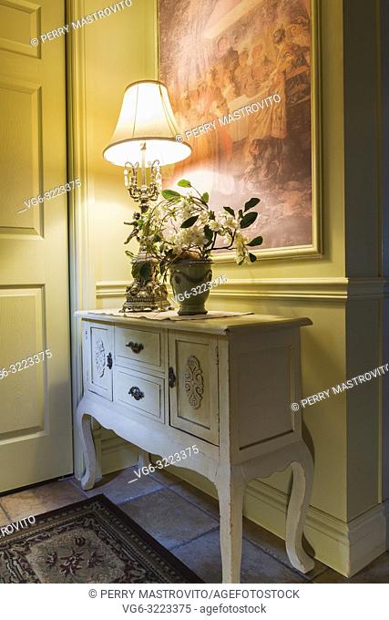 Antique wooden console with lamp and flower vase in the kitchen entryway inside a 2006 reproduction of a 16th century Renaissance castle style residential home