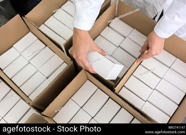 High-angle close-up view of the hands of a manufacturing worker putting packed products, in cardboard boxes before export or shipping during manual work in a...