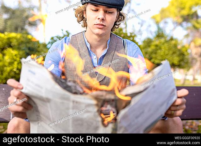 Young man reading lit newspaper while sitting in park