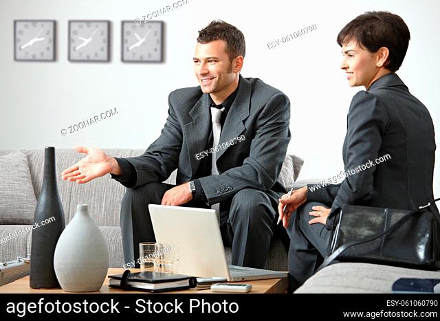 Young business people having meeting at office sitting on sofa talking to partner