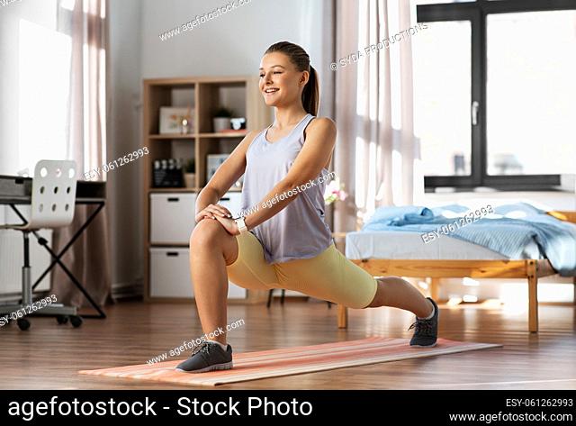 happy teenage girl exercising on yoga mat at home