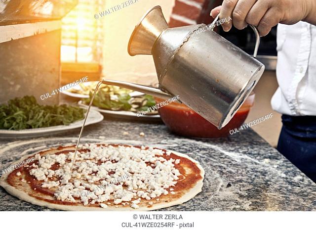 Chef pouring oil on uncooked pizza
