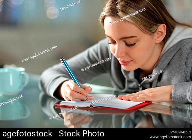 Concentrated teen writing on paper agenda on a table in the night at home