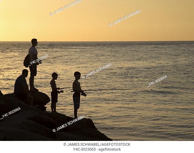 Man and boys fishing in Gulf of Mexico off North Jetty in Nokomis Florida against a orange sunset sky