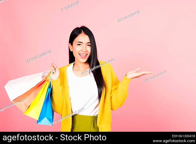 Portrait Asian happy beautiful young woman shopper smiling standing excited holding shopping bags multicolor in summer show something hand palm to copy space
