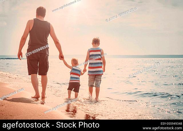Father and sons walking at the beach at sea. A man with children resting at seaside in summer on sunny day