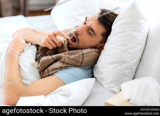 sick man with oral spray lying in bed at home