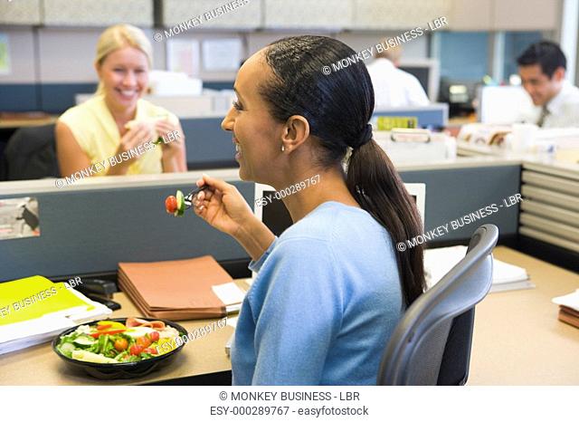 Businesswoman in cubicle eating salad and smiling