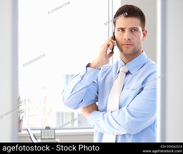 Goodlooking casual office worker talking on mobile phone in bright office