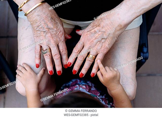 Hand of baby girl pointing on hand of senior woman with rings and red painted nails