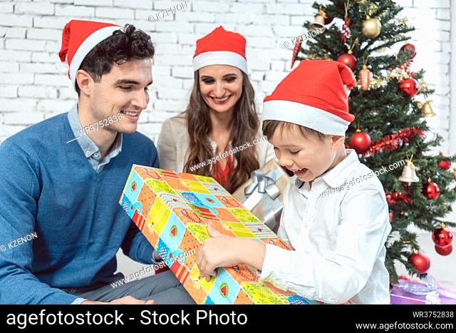 Child unwrapping Christmas present with his family being excited