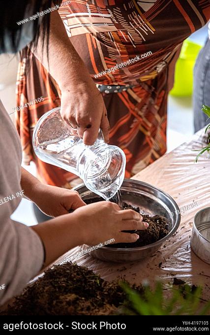 In this captivating image, the hands of a woman delicately cradle a water jug, while another pair of hands support a pot filled with nutrient-rich planting sand