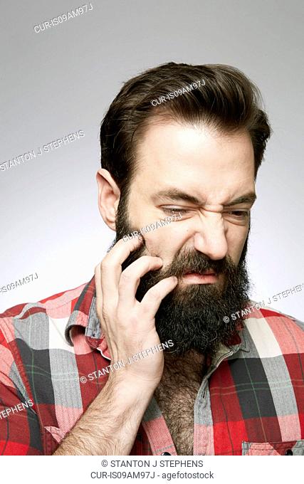 Studio portrait of young man scratching overgrown beard