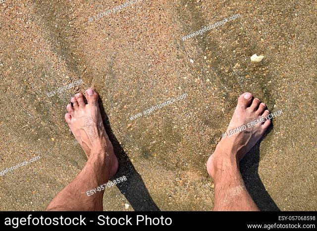 Legs men on the sea sand near sea wave. Walk on the beach