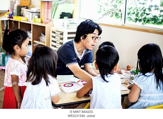 Male teacher talking to group of children at a table n a Japanese preschool