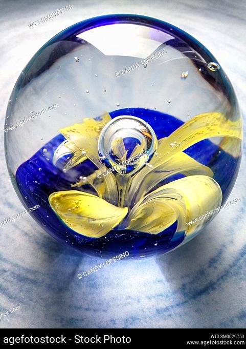 Glass paperweight with yellow flower inside on blue background