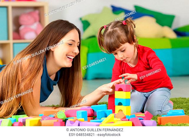 Mother and daughter playing together with colorful construction toys on a carpet on the floor af a bedroom at home