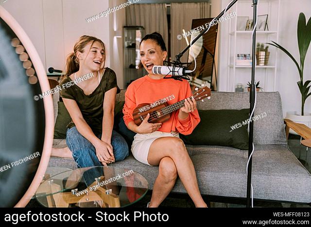 Girl sitting on sofa with female friend playing ukulele at home