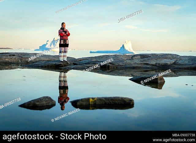 Inuit woman in traditional clothes stands on the shore of Disko Bay on Midsummer, Greenland