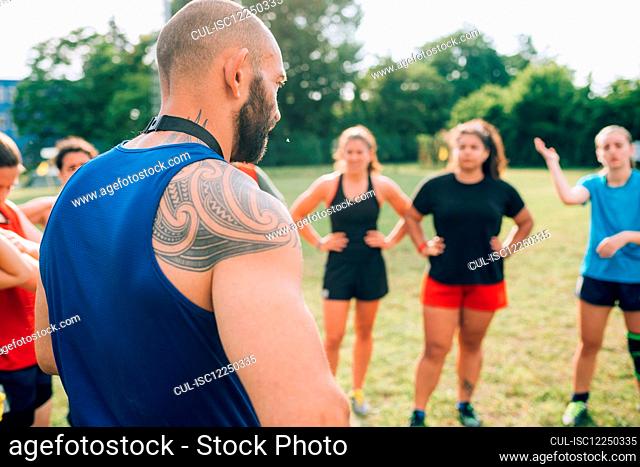 A group of women standing in a circle listening to their male rugby coach