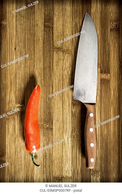 Knife and chili pepper on wooden table