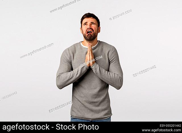 Miserable and distressed young pathetic bearded guy asking mercy, praying god hear prayers, hold hands together over chest, crying and complaining unfair life